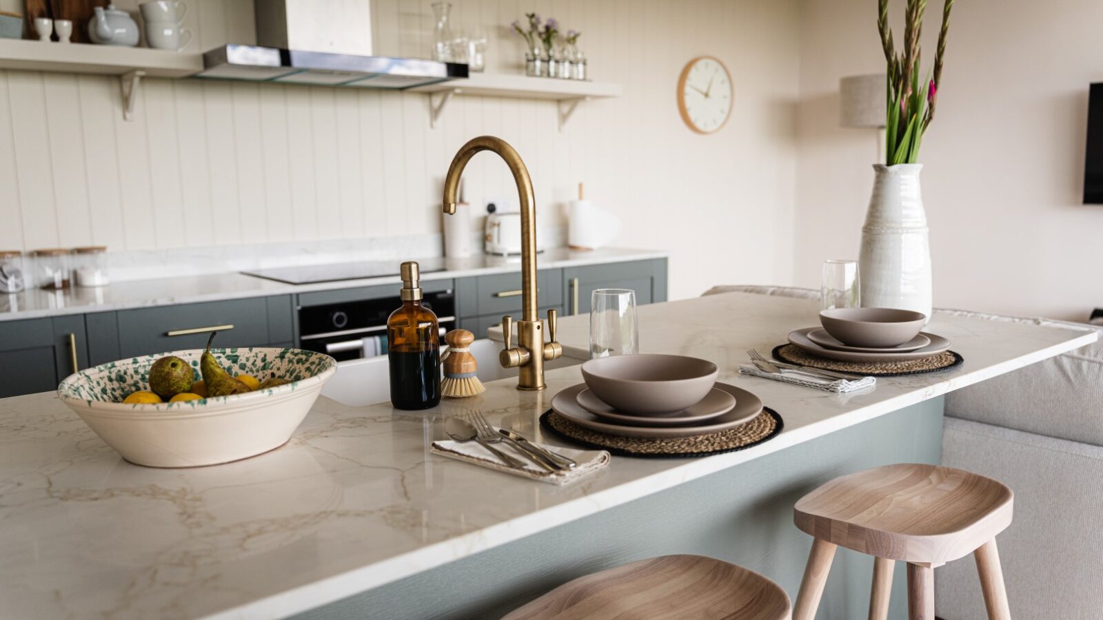 A modern kitchen with a marble island, two place settings, a bowl of lemons, and wooden stools perfectly captures the essence of luxury accommodation. Elegant decor and a gold faucet add the finishing touch to this sophisticated space.