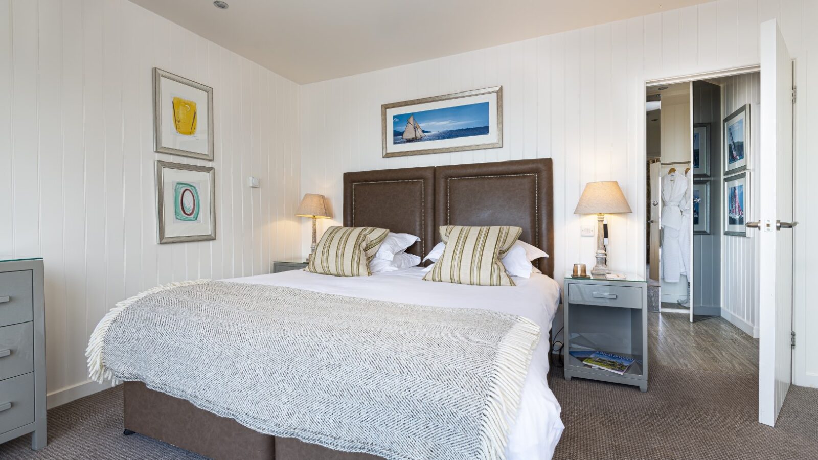 The modern bedroom suite highlights a large bed, two bedside lamps, and framed artwork on the walls, with an open door leading to a sleek bathroom.