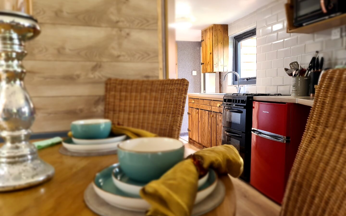 Cozy kitchen space reminiscent of a treehouse with wooden cabinets, red fridge, and a table set for a meal with turquoise dishes and yellow napkins, perfect for an evening spent star gazing through the window.