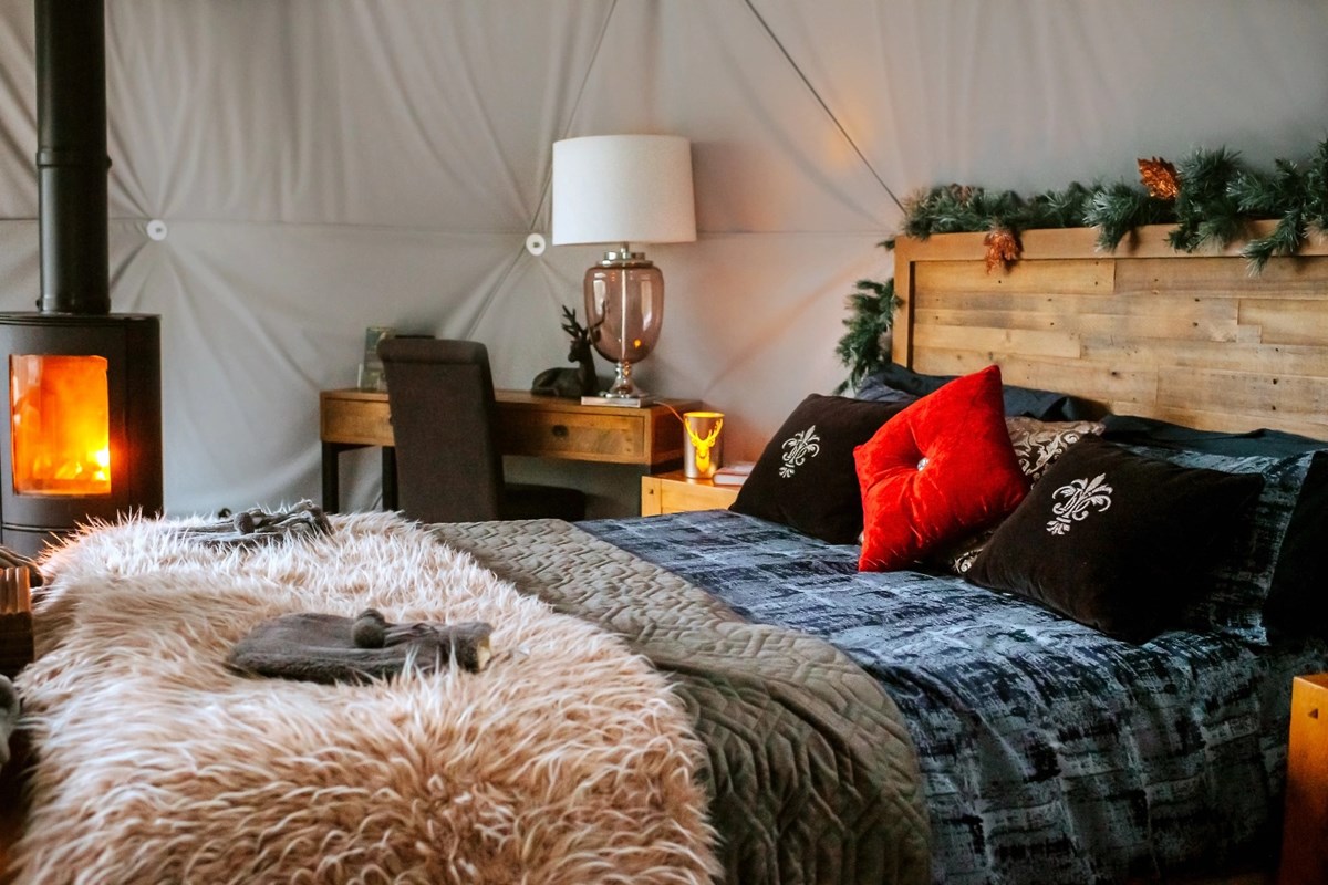 Cozy woodland bedroom with a wooden bed, plush pillows, a soft throw, a desk, and a warm fireplace, decorated with greenery garland.