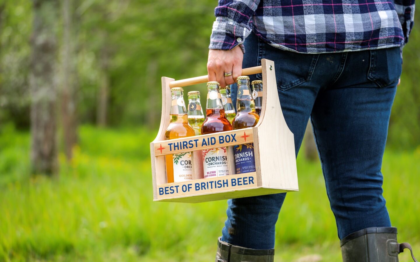 A person wearing jeans and a plaid shirt carries a wooden crate labeled 