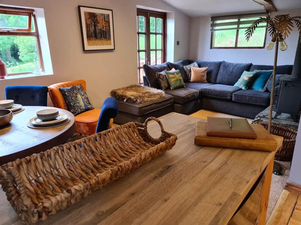 Cozy living room with a sectional sofa, wooden table, and wicker basket exudes the charm of lodges. The dining set by the window offers enchanting outdoor views, perfect for woodland escapes.