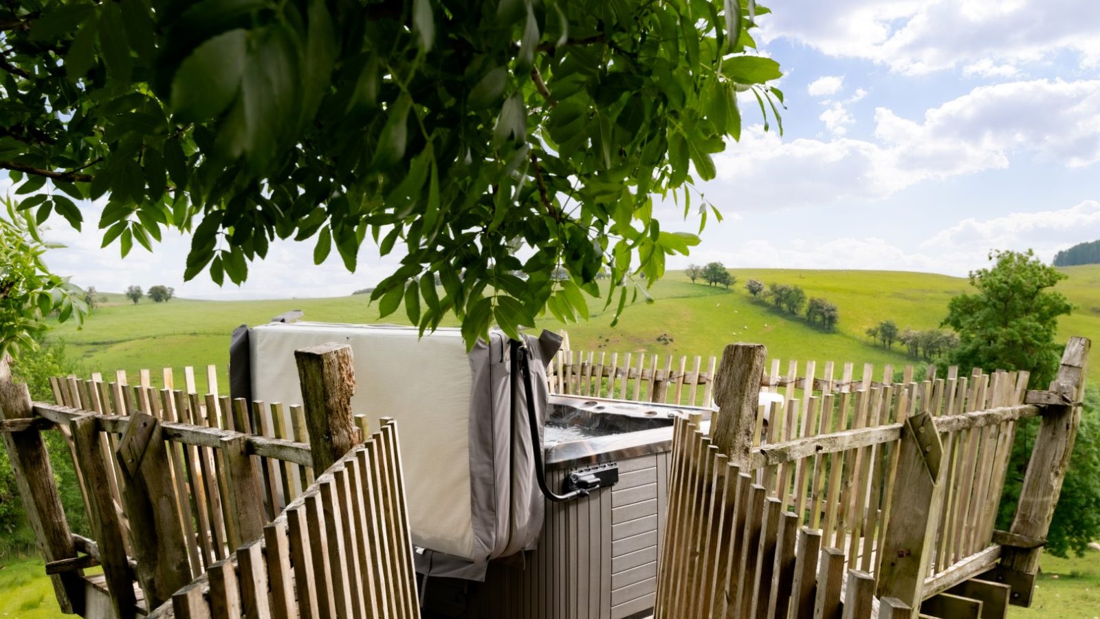 A hot tub on a wooden deck offers an idyllic escape with its scenic view of rolling green hills under a partly cloudy sky. Perfect for those seeking cheap breaks with hot tubs in the UK, this spot provides relaxation and natural beauty without the hefty price tag.