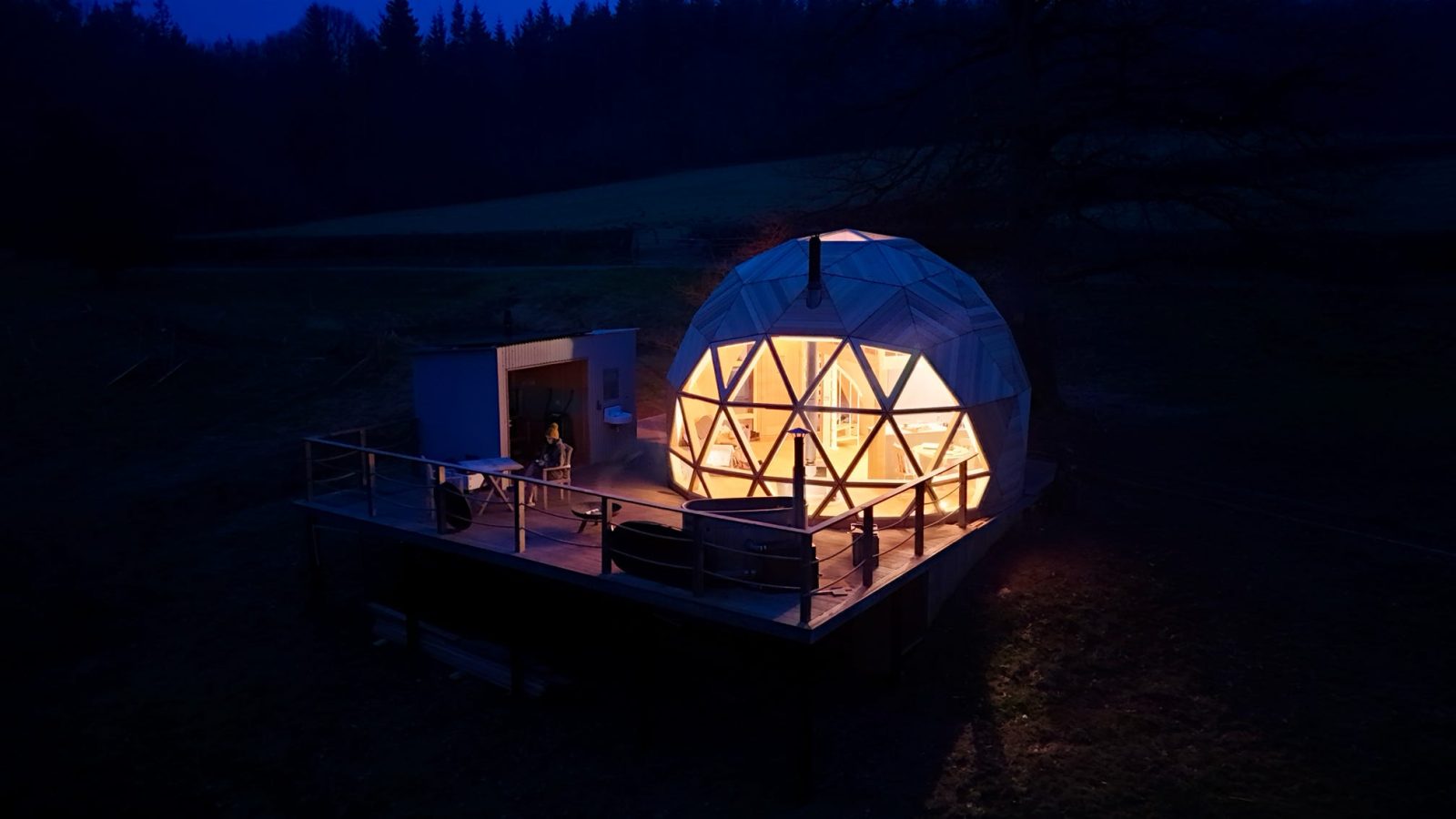 The Nova Dome at The Fold glows brilliantly on a wooden deck amidst a shadowy nighttime landscape.