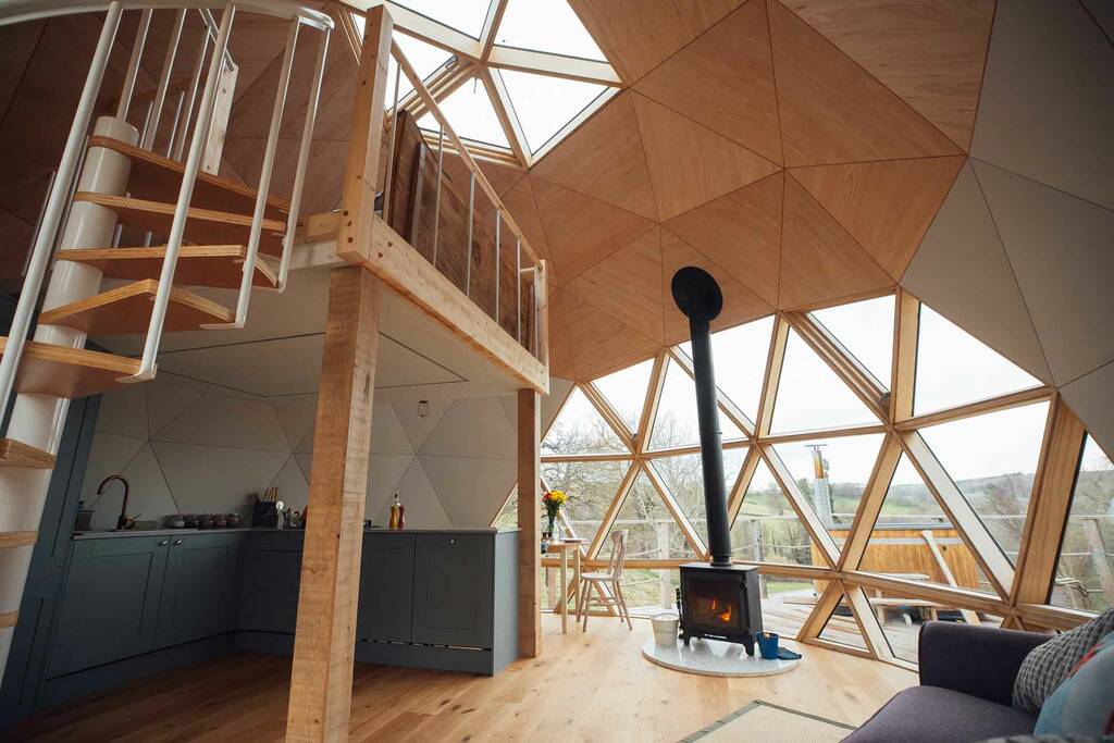 The Nova Dome at The Fold features wooden floors, a spiral staircase, a wood stove, and large triangular windows.