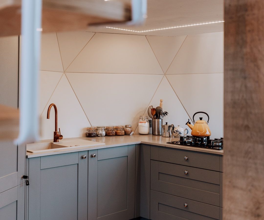 Modern kitchen corner in The Nova Dome with light blue cabinets, a wooden countertop, and a black gas stove with a kettle.