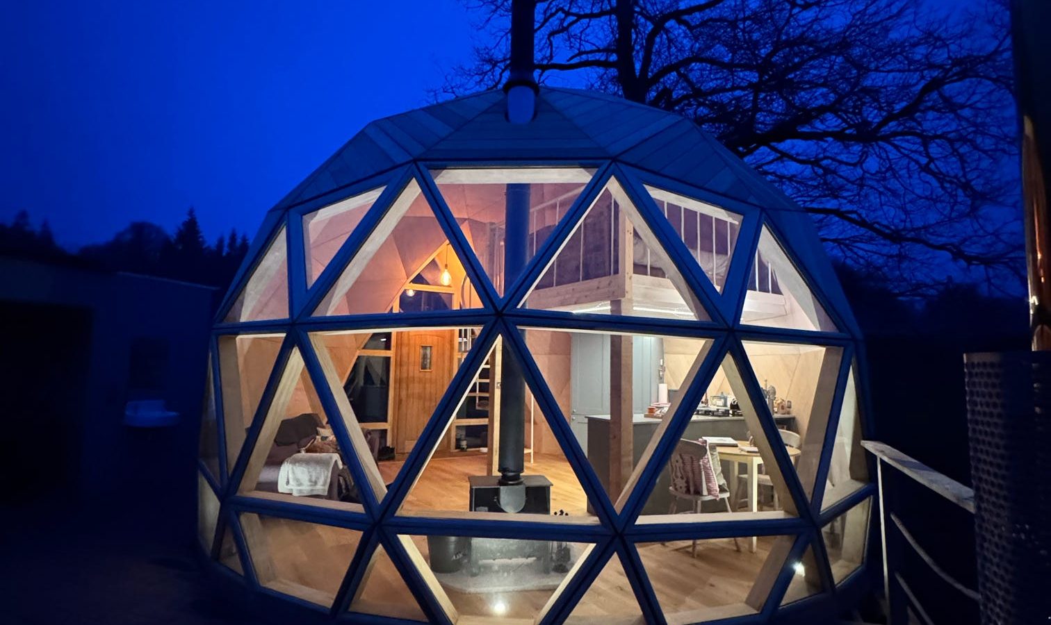 The Nova Dome at The Fold, lit from within, reveals a tree silhouette against the twilight sky.