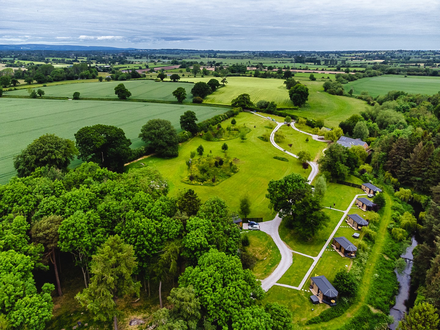 Aerial view of Shropshire’s rural landscape with green fields, scattered trees, winding paths, and houses near a river.