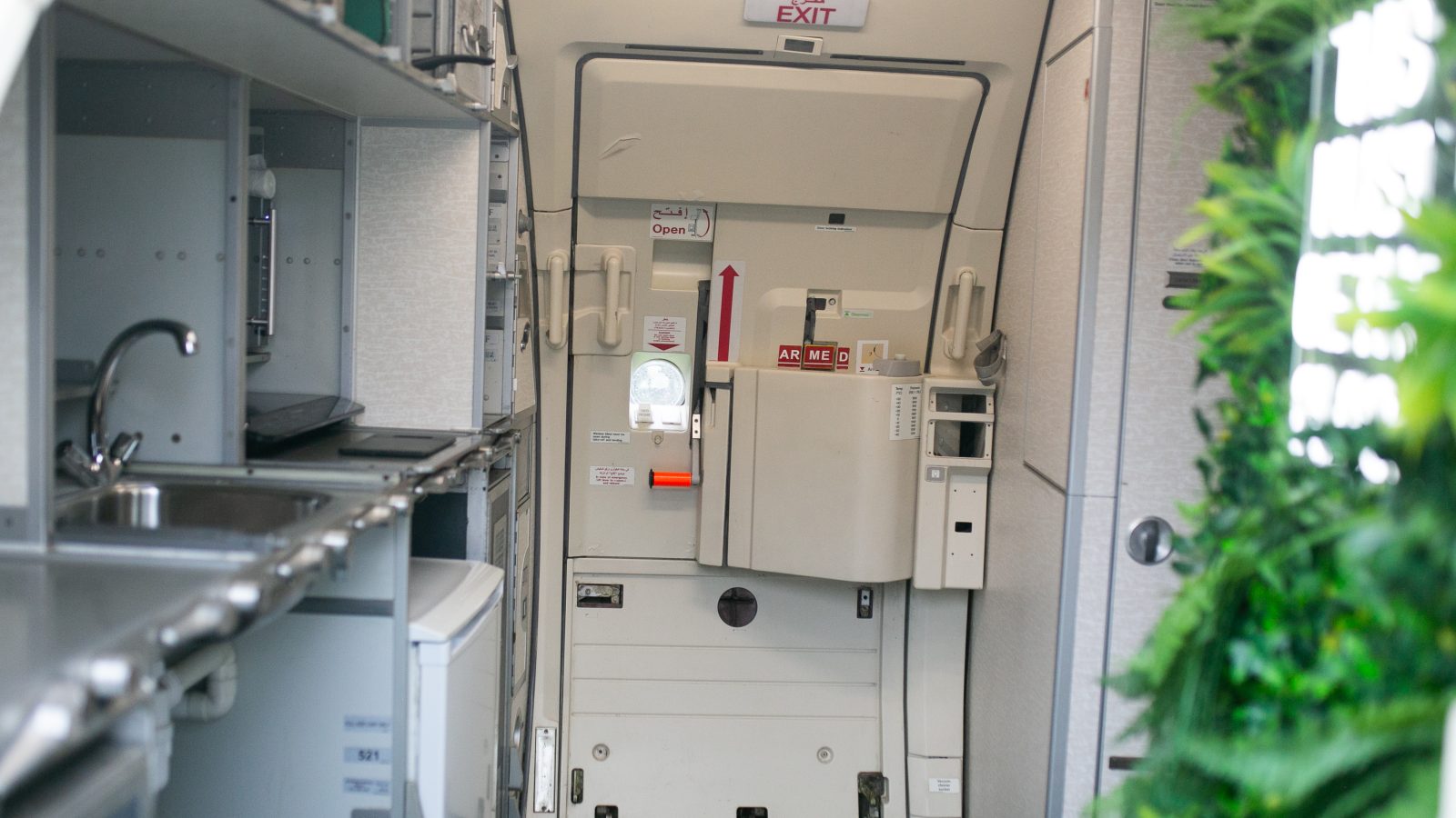 An airplane's rear galley and exit door. The galley, essential for flight attendants on jets, features various storage compartments, a sink, and other equipment. The exit door has a red handle and an 