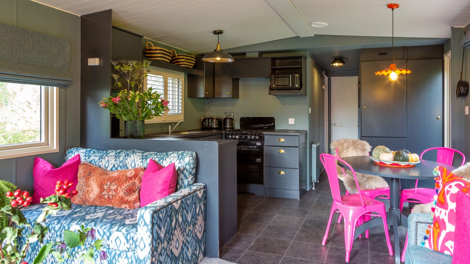 Modern accommodations featuring a patterned sofa, colorful decor, a dining table with pink chairs, and a compact kitchen create an inviting atmosphere reminiscent of Howgill Lodge.