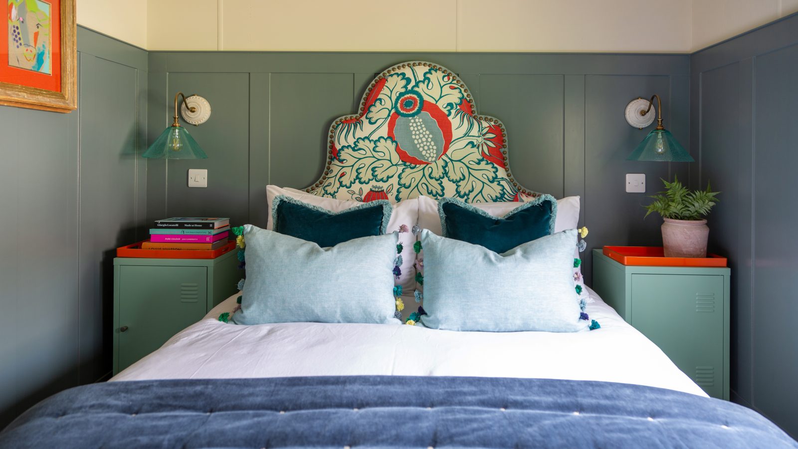 A neatly arranged bed with a colorful headboard, decorative pillows, and side tables adorned with books and potted plants create a cozy ambiance at Howgill Lodge.