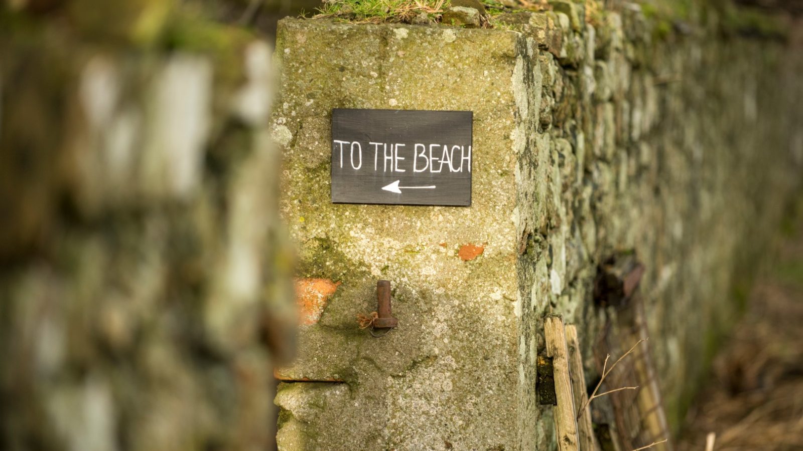 A stone wall with a black sign reading 