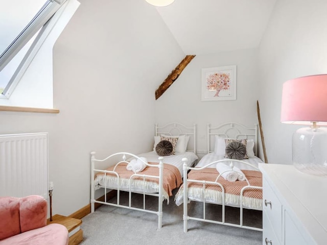 A cozy attic bedroom with two white-framed single beds adorned with peach-colored blankets and decorative pillows. A framed Penshenkin art piece hangs above the beds, and a slanted window allows natural light to flood in, highlighting a pink lamp and a pink plush chair in this charming barn-like retreat.