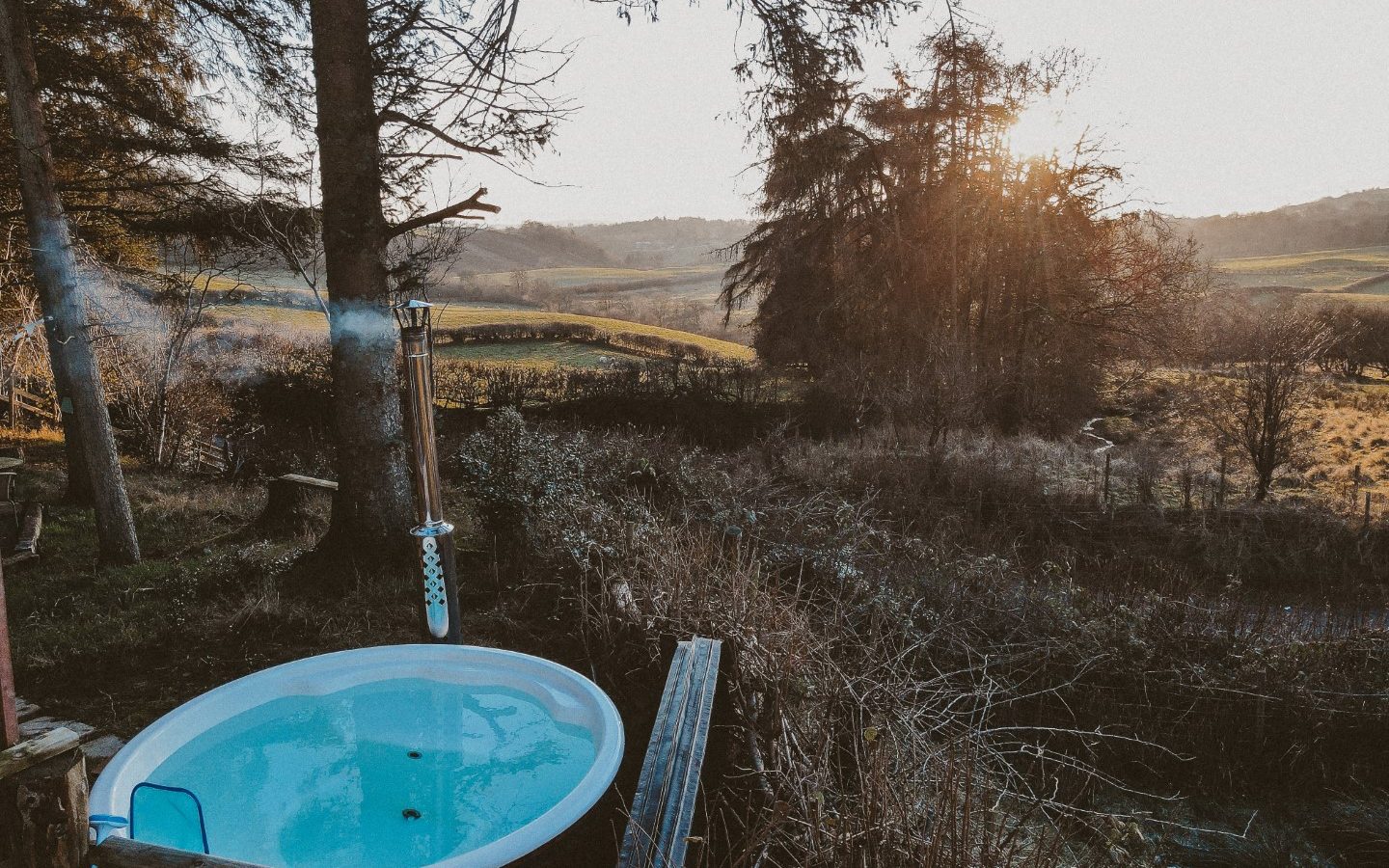 Enjoy a relaxing soak in the outdoor hot tub of your tiny house, nestled in the woods. Experience breathtaking views of the rural landscape at sunset, surrounded by serene trees and expansive fields.