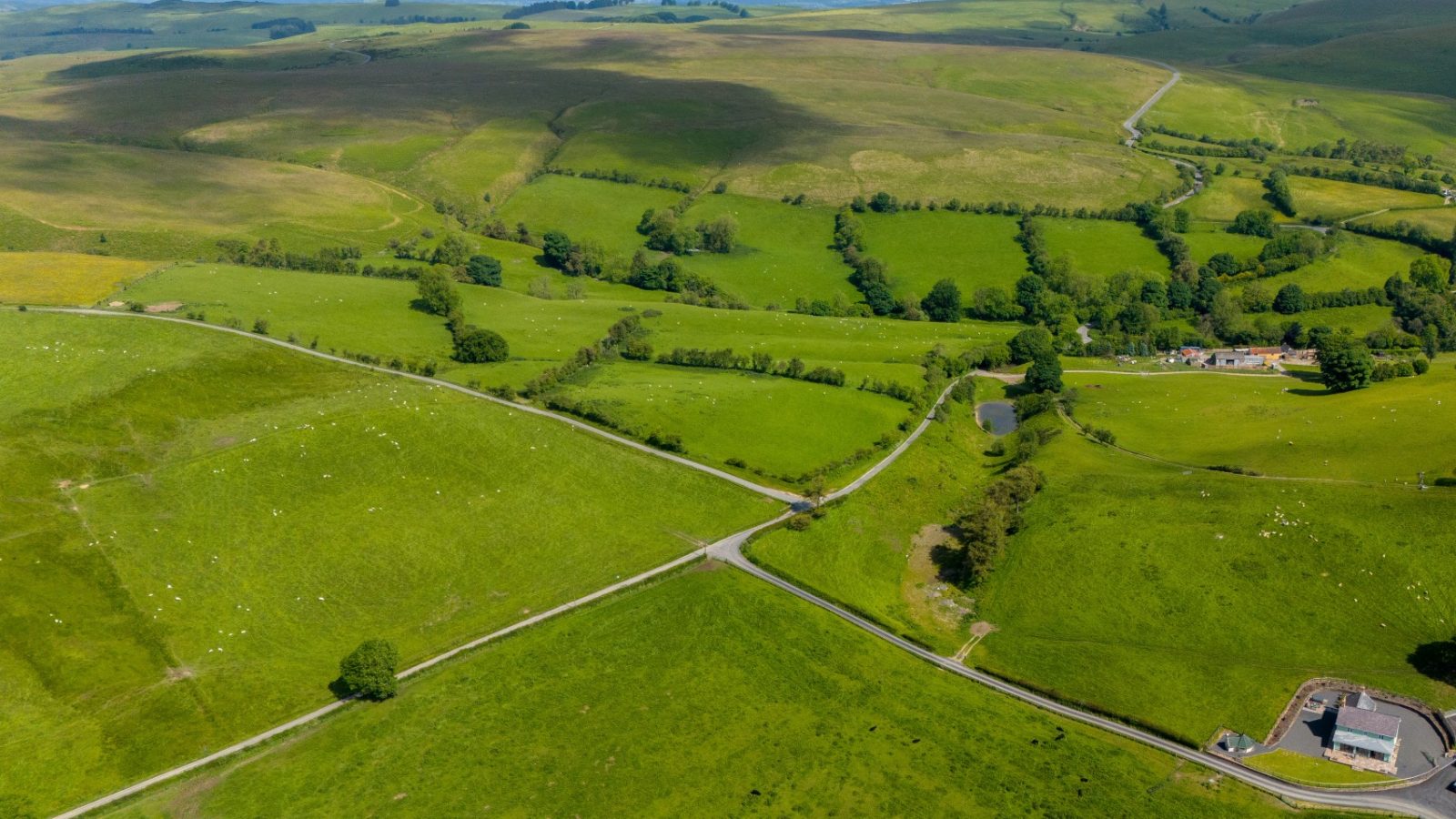 Aerial view of a lush, green rural landscape with rolling hills, intersecting roads, and scattered trees. Small clusters of buildings and farmland are visible, with Waen Farm House standing prominently. A gentle river winds through the scene under a partly cloudy sky.