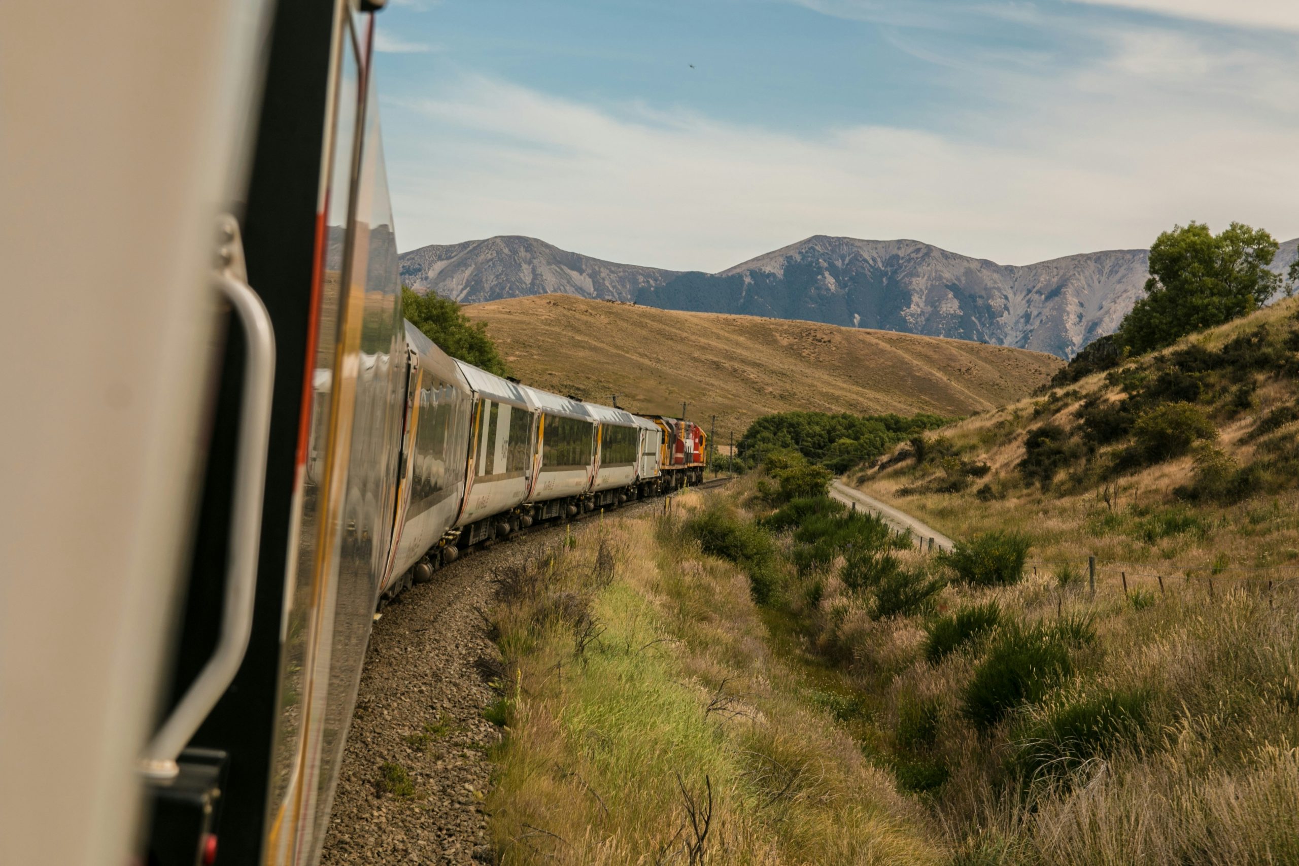 A guide to North Wales: A train journeys through grassy mountains under a cloudy sky, viewed from a trailing car window.