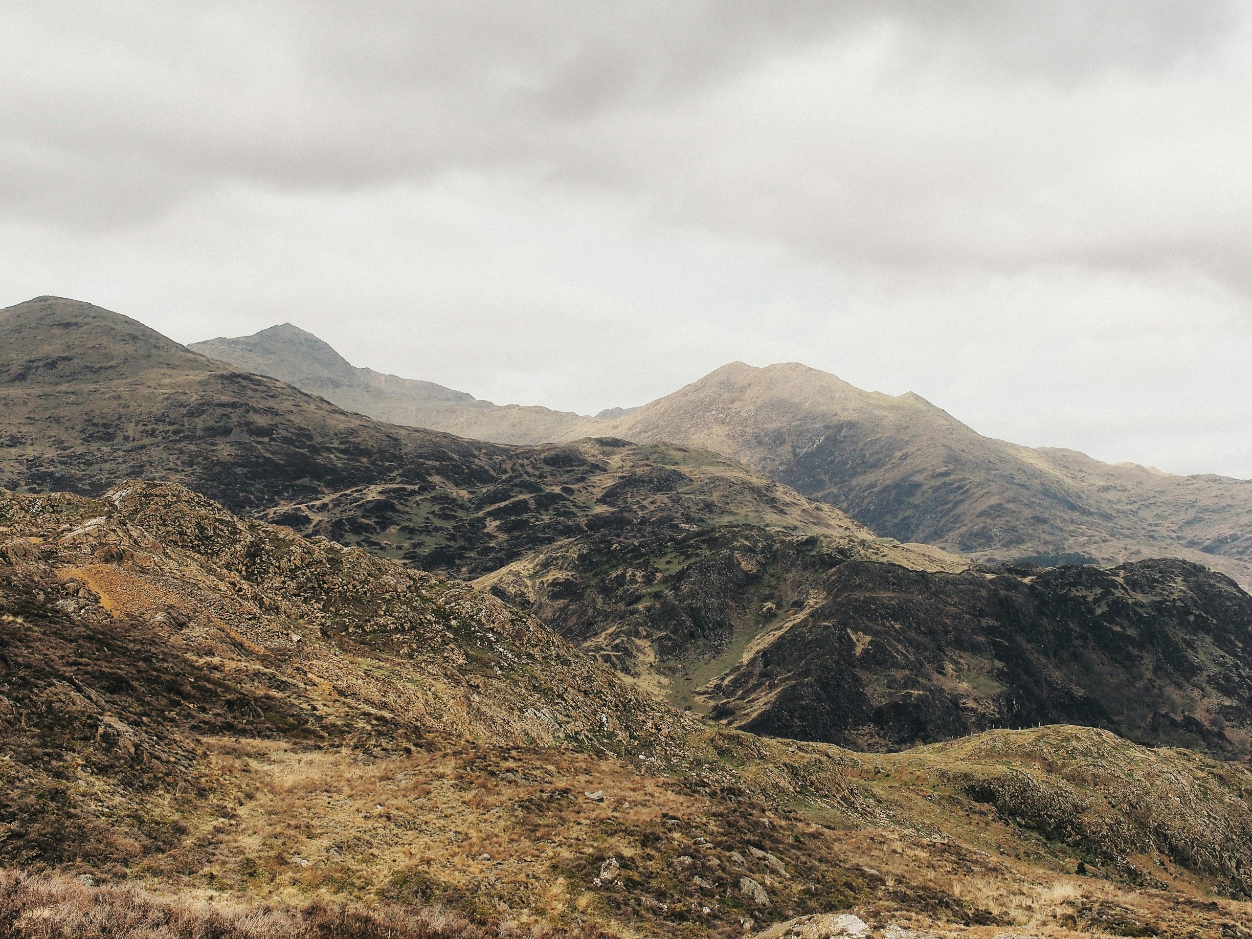 Hazy sky over rocky, grassy hills under an overcast sky—a scenic glimpse from A Guide to North Wales.