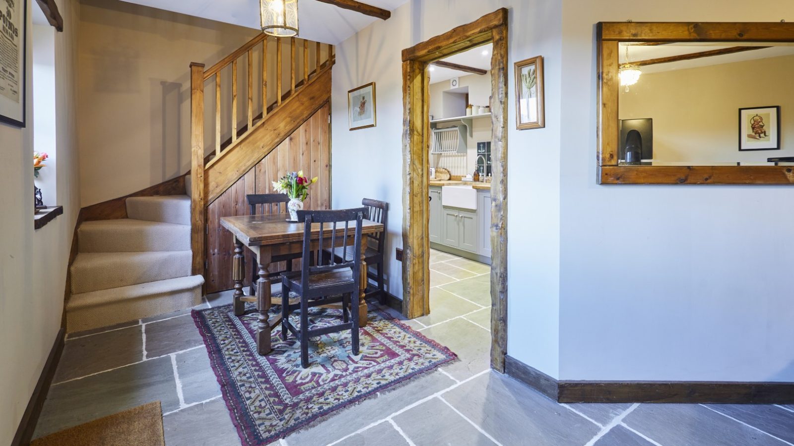 Cosy dining area at Gablebach, with a wooden table and chairs, a staircase, and wall-adorned mirror and framed pictures. An ideal romantic country cottage getaway