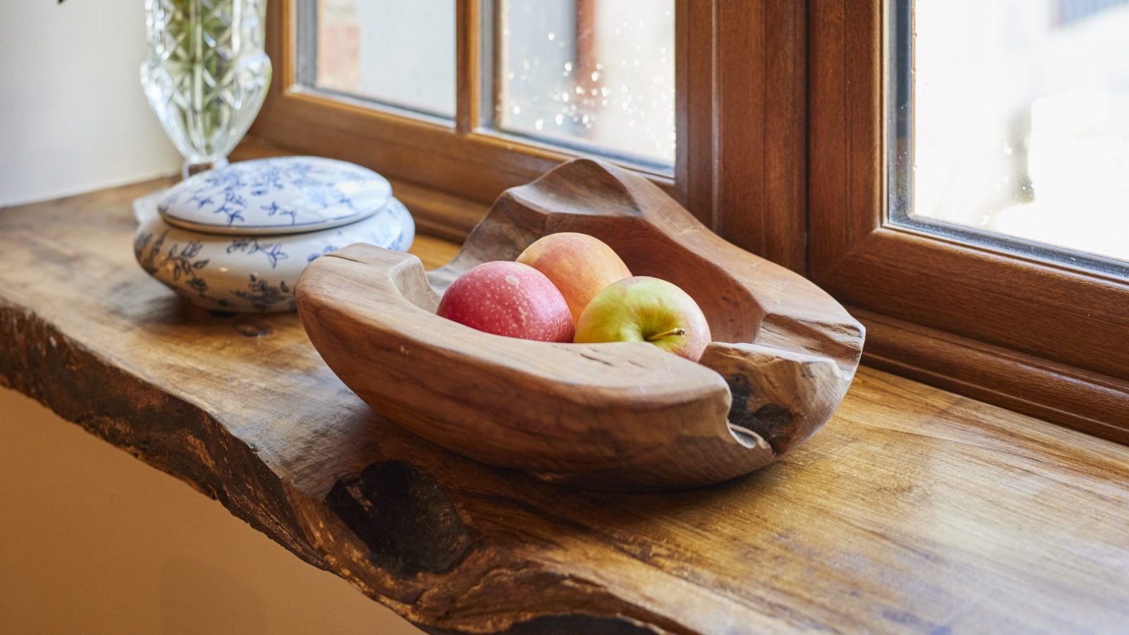 A wooden bowl with three apples rests on a windowsill at Gablebach, next to a ceramic container.