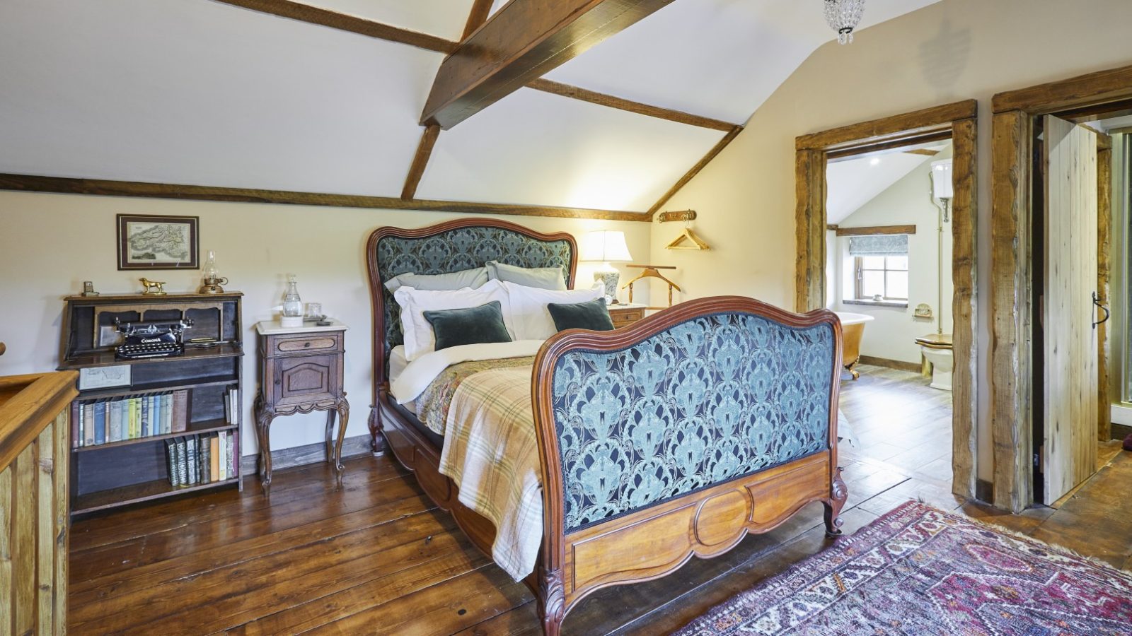 A cosy bedroom at Gablebach, featuring a vintage wooden bed, bookshelves, and exposed beams; a hallway is visible.