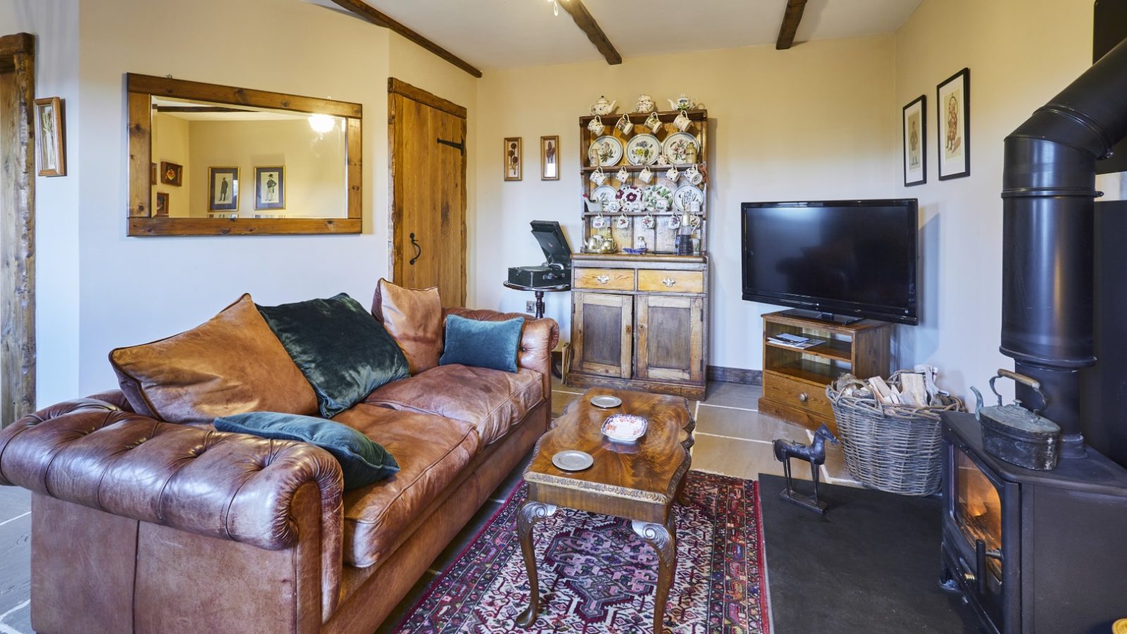 Cosy living room with a leather sofa, wooden furniture, TV, wood-burning stove, and decorative plates. Gableback at Black Mountain Escapes