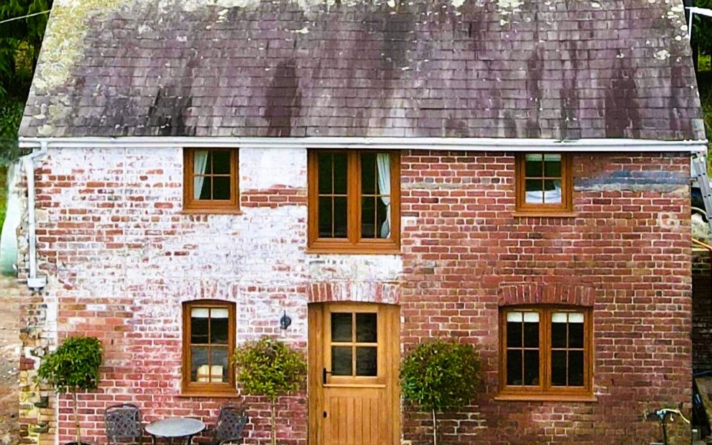 A small, rustic brick cottage, Gablebach at Black Mountain Escapes, with a weathered roof and potted plants by the entrance.