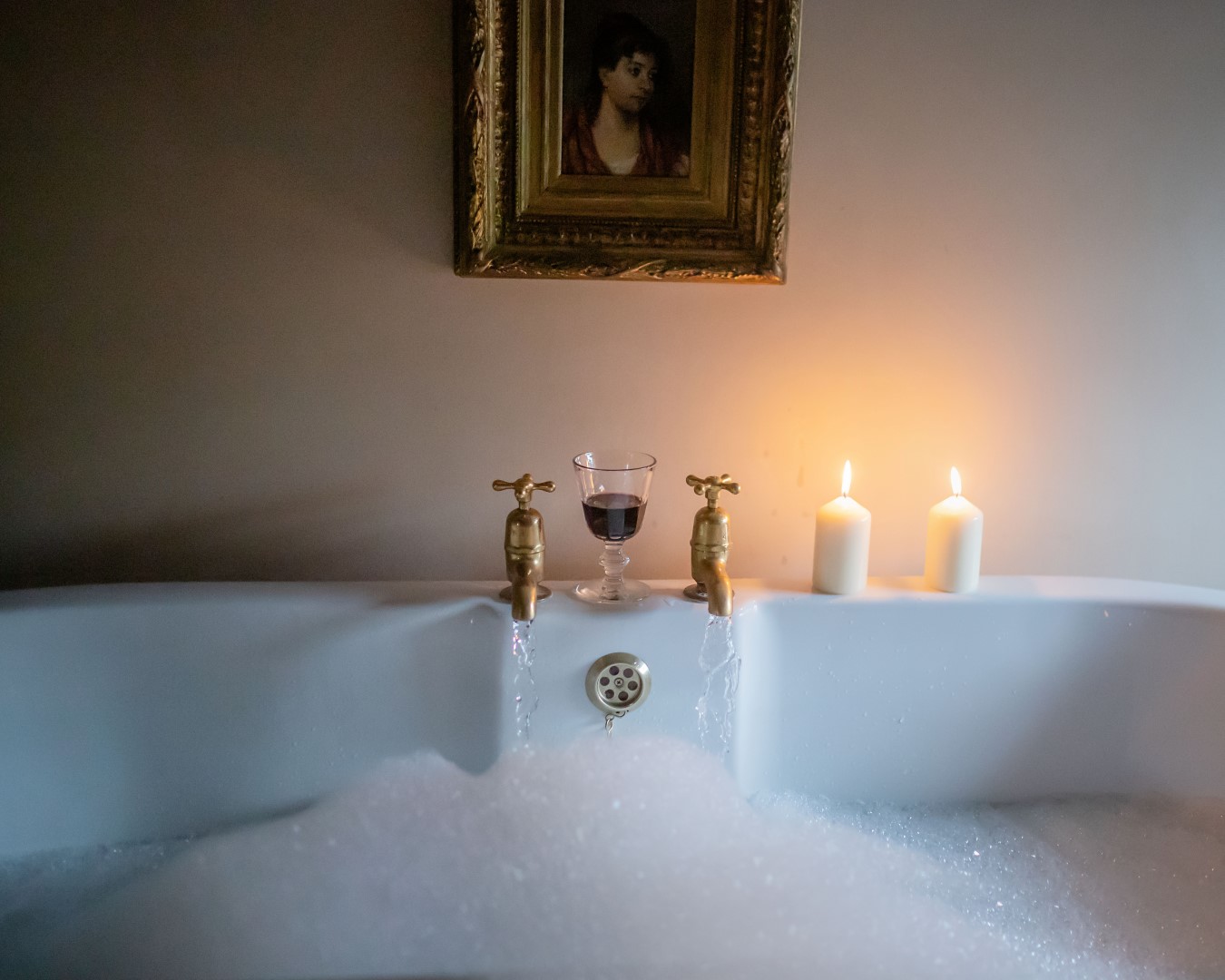 A bubble bath with two lit candles, a glass of red wine, and a framed portrait above the tub offers the ultimate relaxation experience. It's just like being at Black Mountain Escapes, where tranquility meets indulgence.