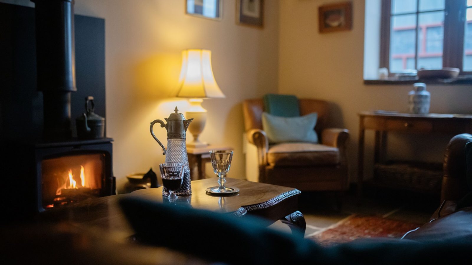 Cosy living room at Gablebach, Black Mountain Escapes, with a lit fireplace, armchair, decanter set, and warm lamp. Perfect for a romantic getaway for two