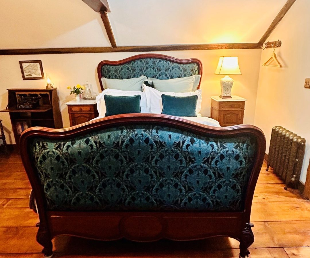 A cozy attic bedroom in Black Mountain with a wooden and upholstered bed, patterned rug, bedside tables with lamps, and a radiator. Perfect for those seeking comfort at Black Mountain Escapes.