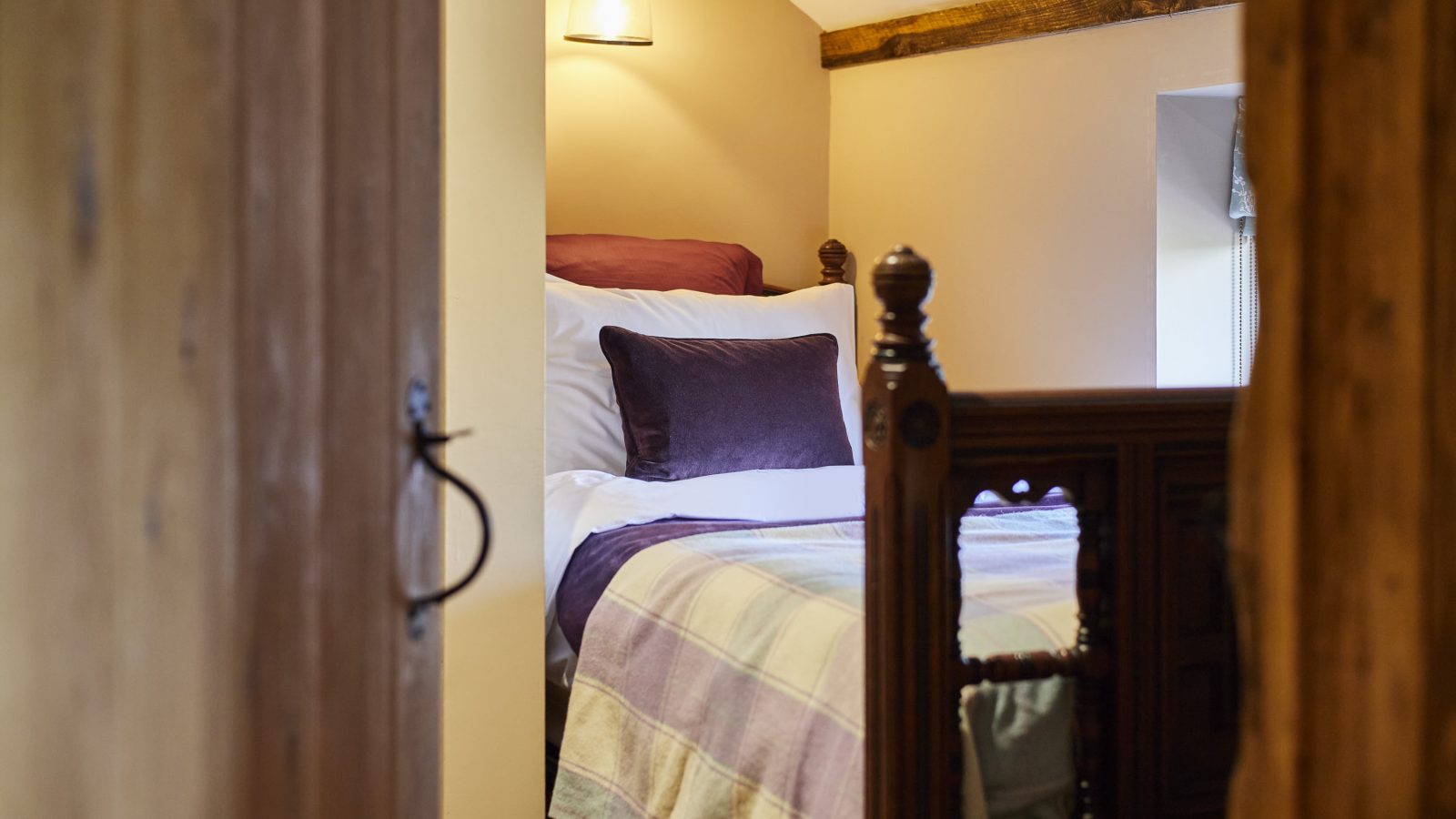 Cozy bedroom with a neatly made bed, wooden headboard, and soft lighting, viewed through an open door at Black Mountain Escapes.