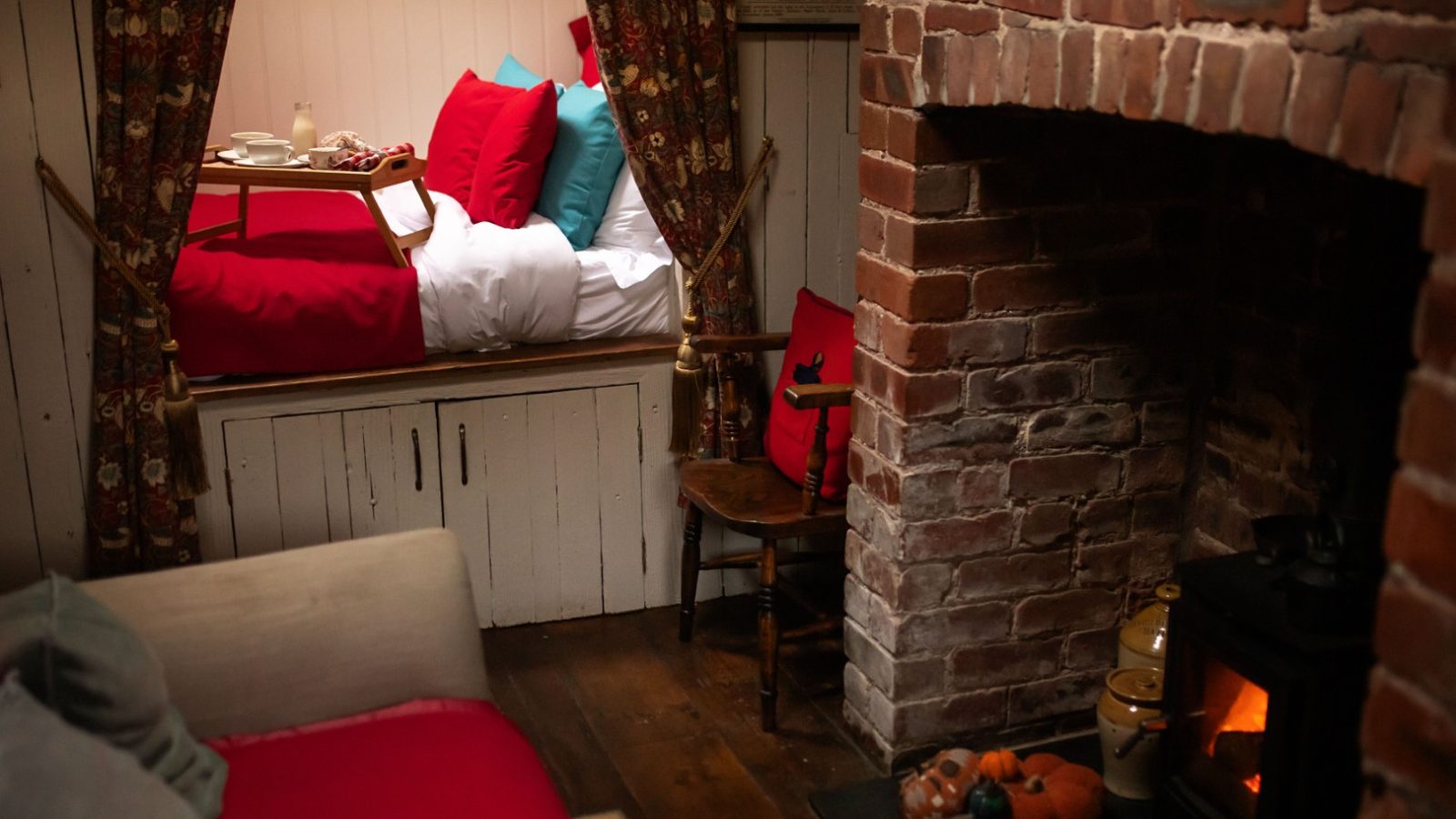 A Cosy room with a bed, colourful pillows, breakfast tray, brick fireplace, and decorative items on the floor at Y Golchdy at Black Mountain Escapes