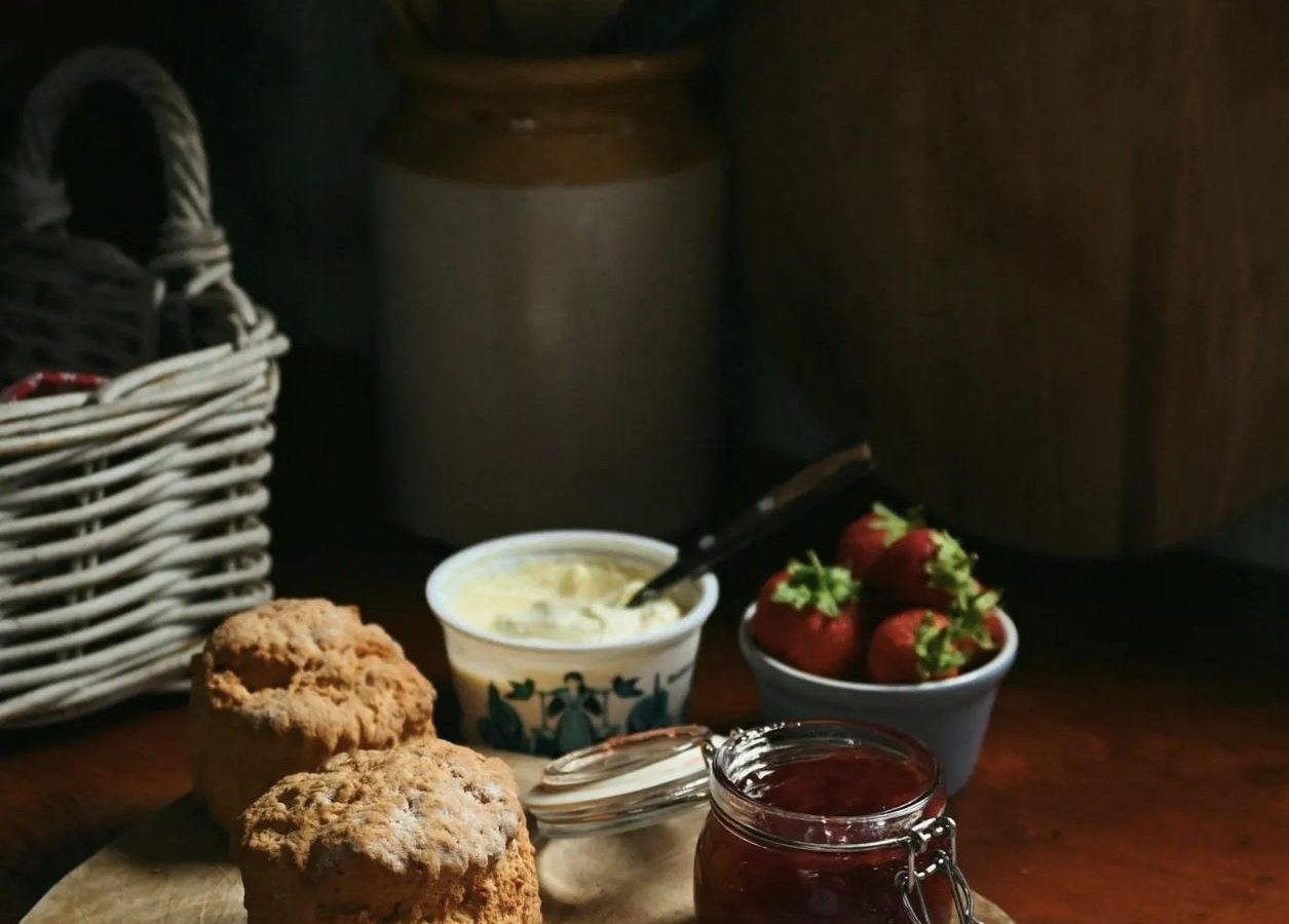 Scones on a wooden board with a jar of jam, a bowl of strawberries, and a pot of cream create a cozy scene at Black Mountain Escapes, set on the rustic kitchen table of Y Golchdy.