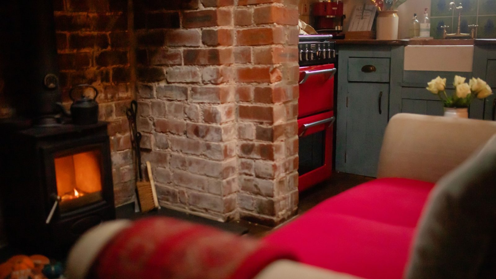 Cosy living space with brick fireplace, red stove, and blue cabinets at Y Golchdy at Black Mountain Escapes