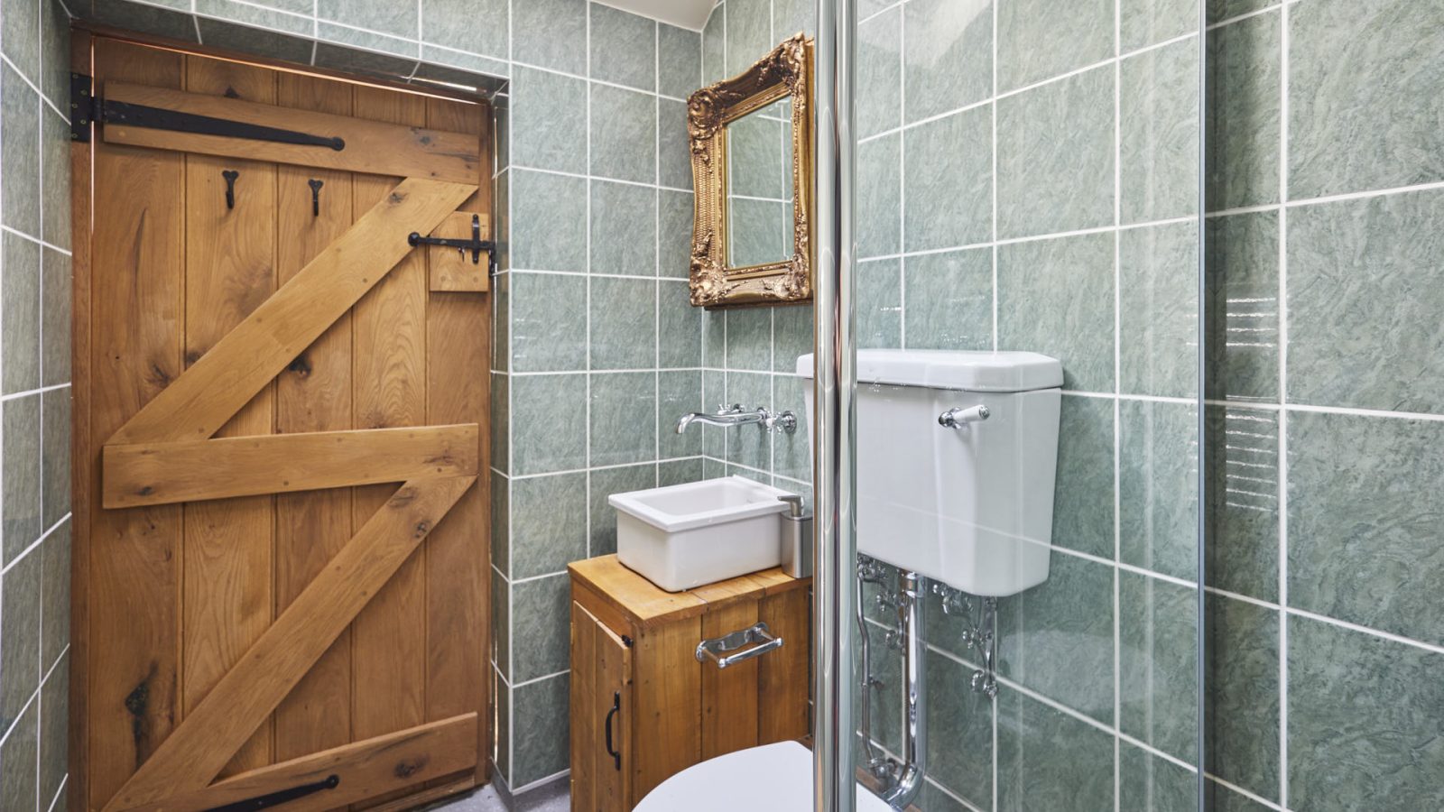 Cosy bathroom at Y Golchdy, Black Mountain Escapes: green tiles, wooden door and cabinet, mirror, white toilet, and small sink.