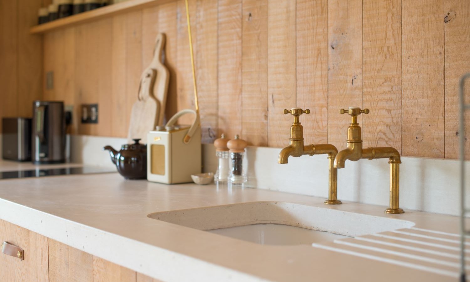 A cozy kitchen countertop in the charming Holly Water Cabin, adorned with wooden paneling, brass faucets, a cutting board, a teapot, and various kitchen items. The bright space exudes a warm, rustic vibe.