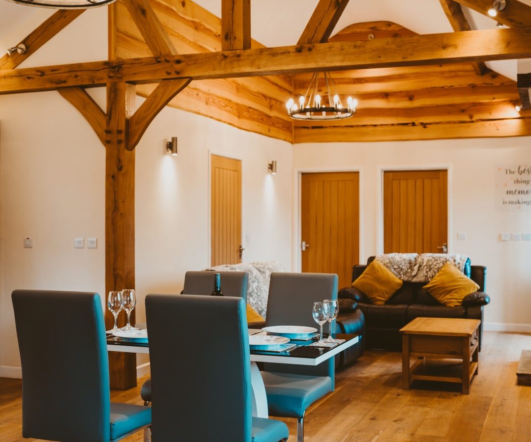 Rustic living room and dining area with exposed wooden beams, modern furniture, and wood flooring at Ploony Holidays Wales.