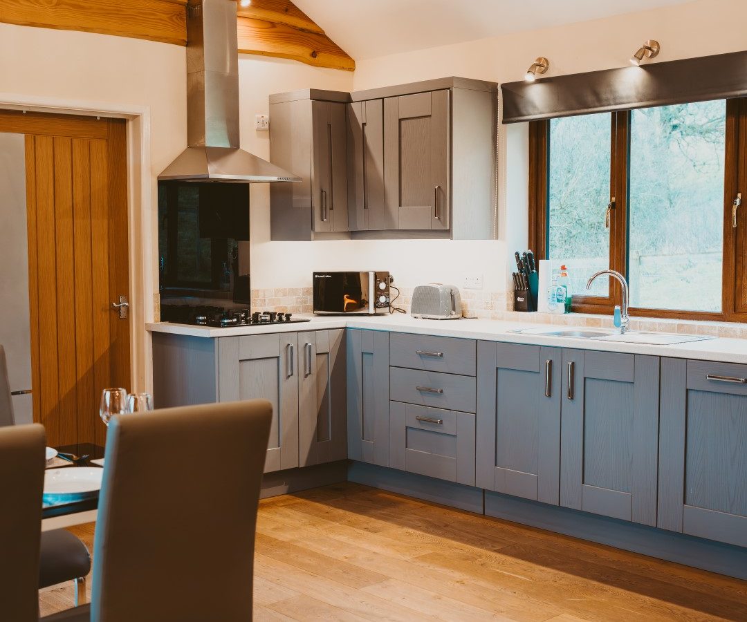 Modern kitchen with gray cabinets, wooden flooring, dining table, large windows, and a chandelier perfect for Ploony holidays.