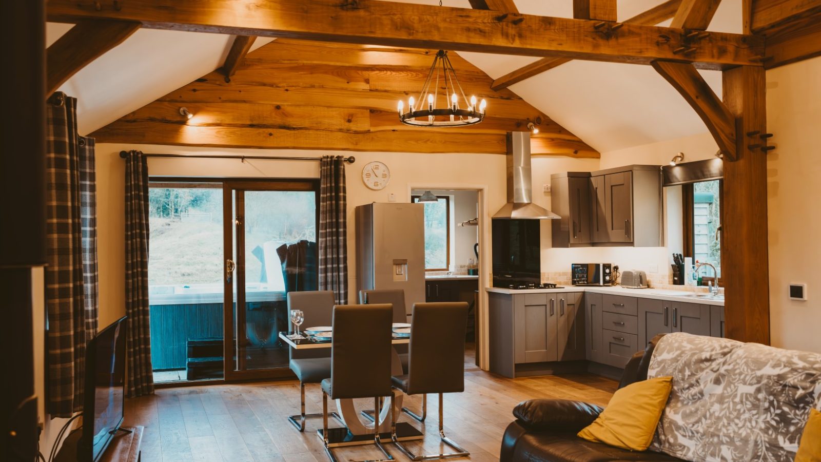 Cosy living room with wooden beams, modern kitchen, and dining area. Ideal for Ploony Holidays Wales getaways.