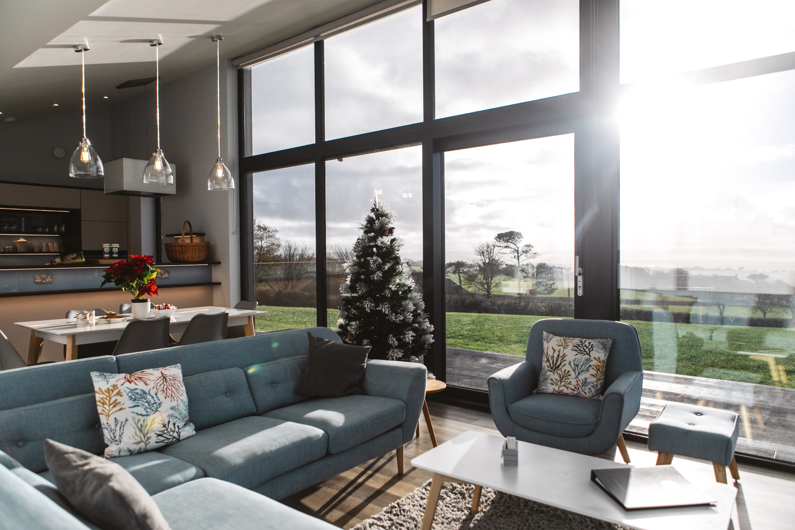 Modern living room with large windows, blue sofas, and a Christmas tree, offering a perfect spot for Christmas family breaks in the UK, enhanced by the view of greenery outside.