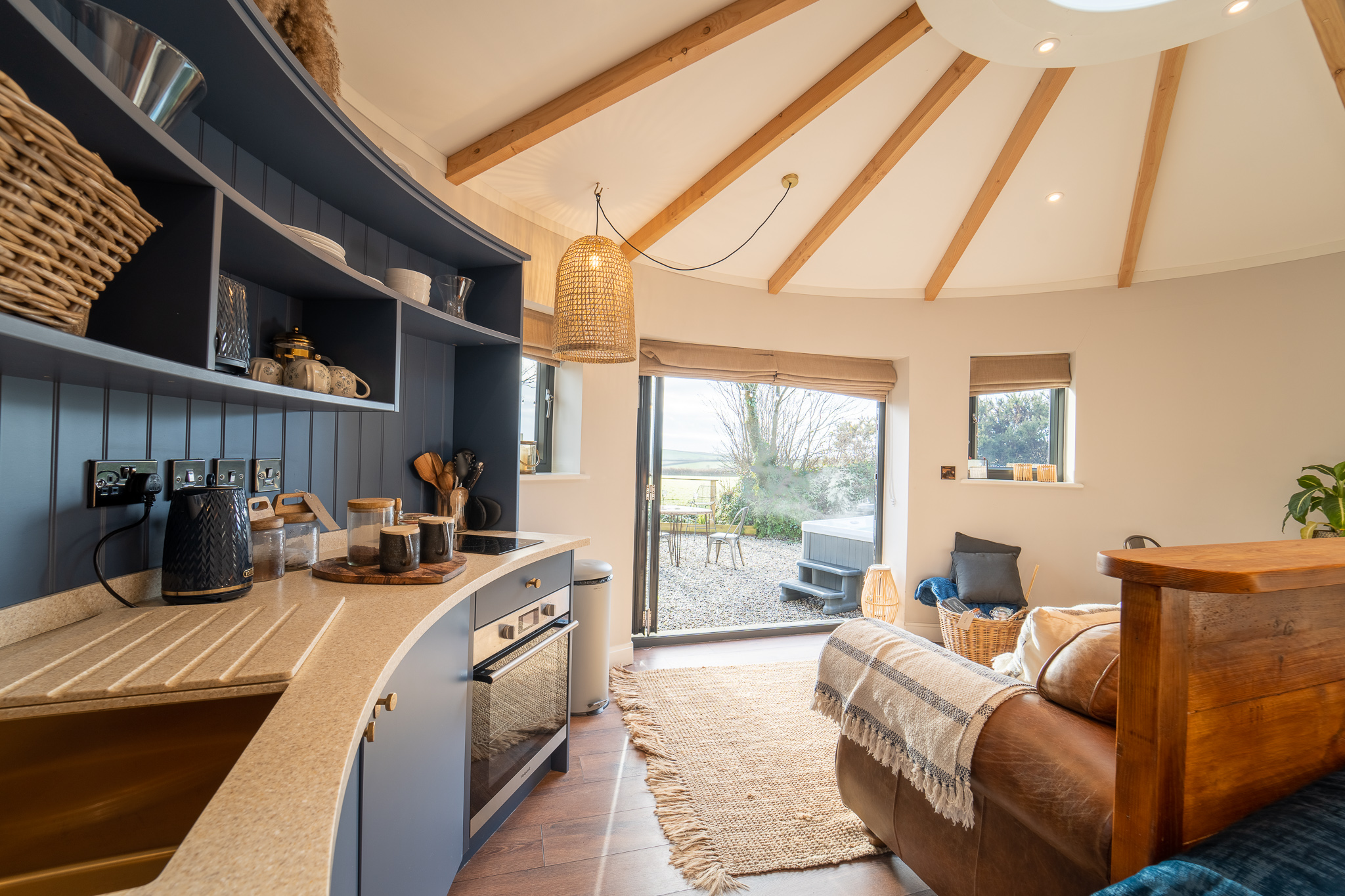 Interior of a cozy round cabin with a modern kitchen and open doors revealing the scenic beauty reminiscent of Coastal Cornwall. Warm, natural decor elements create an inviting atmosphere, perfect for relaxing UK breaks.