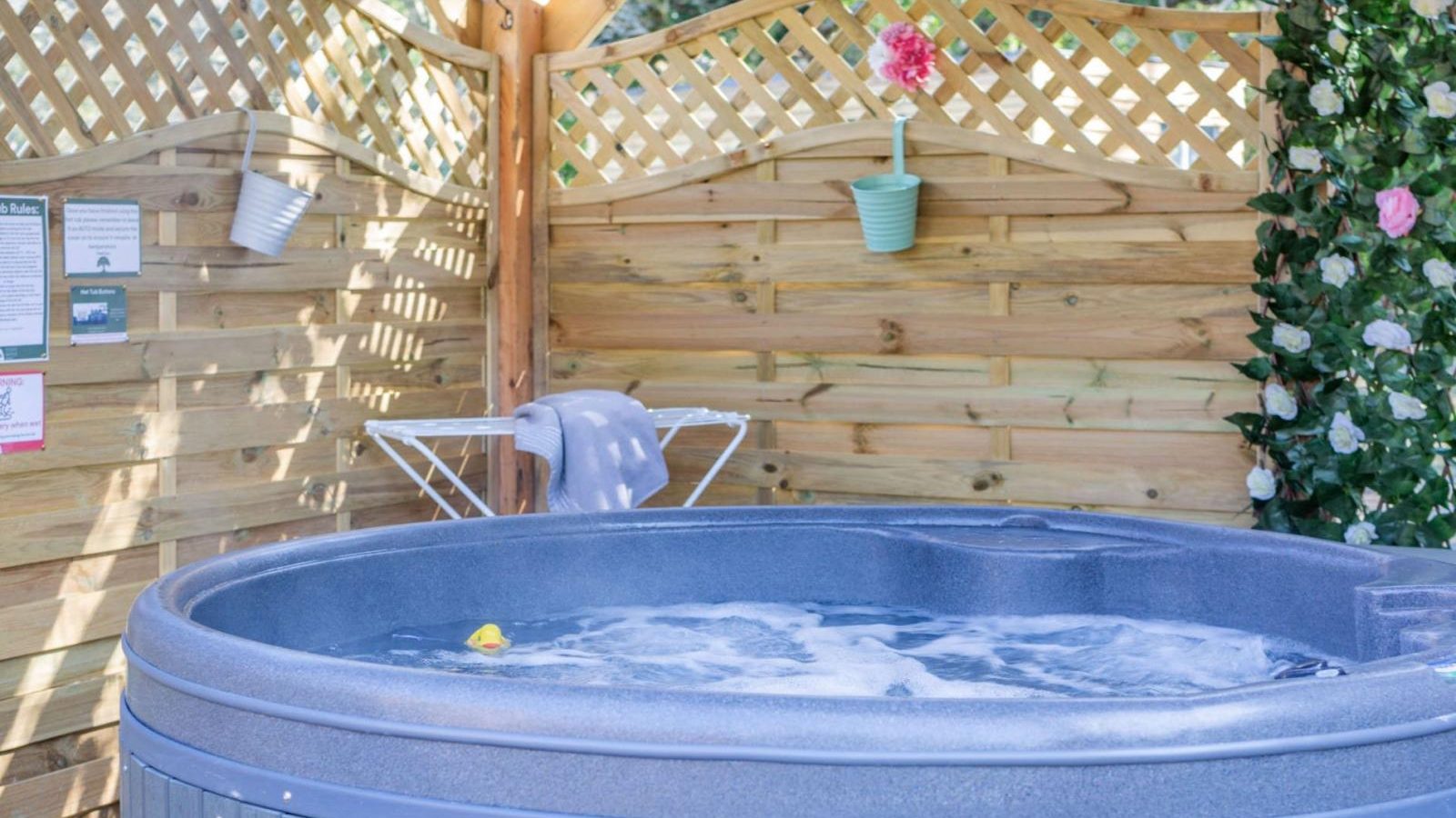 An outdoor hot tub in a wooden gazebo offers a hidden retreat with bubbles, a rubber duck, and a towel on the side. A trellis adorned with plants enhances this glamping experience.