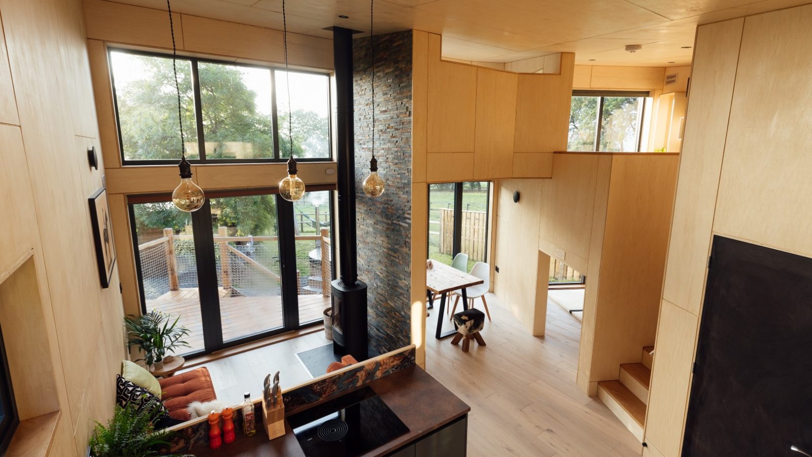 Modern TreeTops interior with wood paneling and large windows, a cozy seating area, and a central brick column adorned with hanging lights.