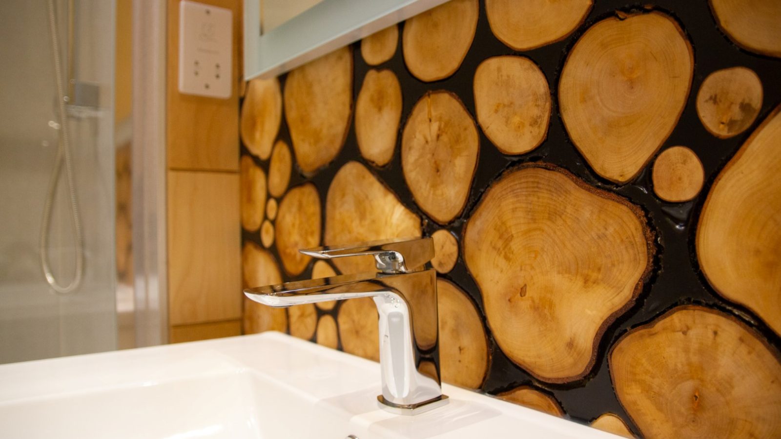 The Bathroom sink with a modern chrome faucet is beautifully complemented by the decorative wall featuring Orcop TreeTops wood slice patterns with a resin or dark filler.