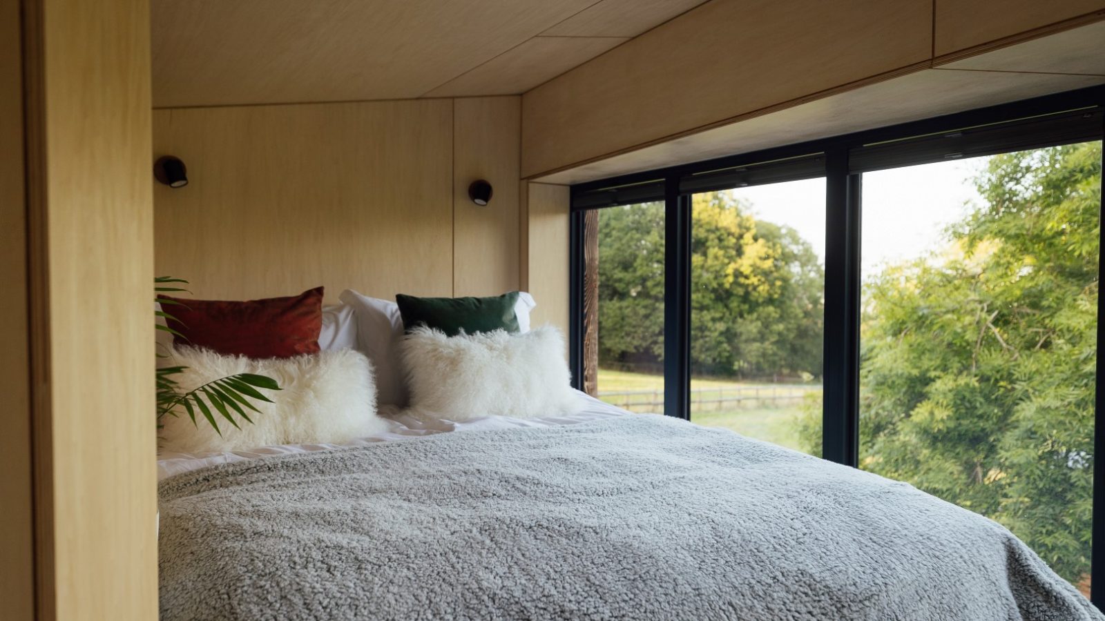 Cozy bedroom with a large window overlooking the Orcop treetops, featuring a neatly made bed with fluffy pillows and a soft blanket.