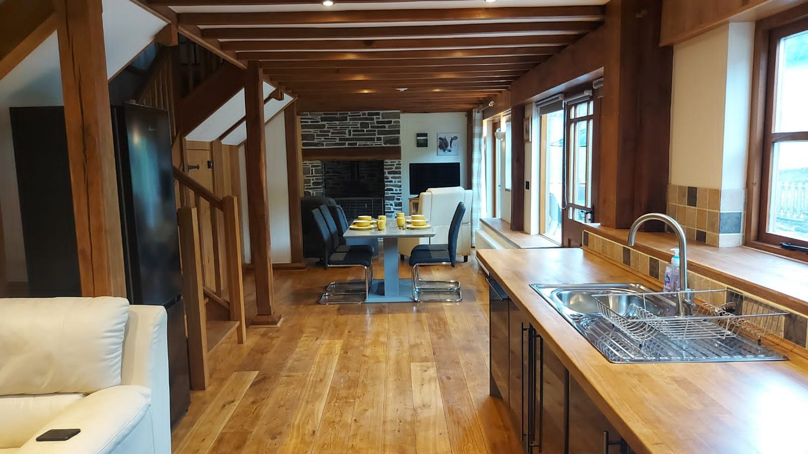 Experience a modern open-plan kitchen and dining area at Ploony Holidays in Wales, featuring wooden floors, exposed beams, and a cozy fireplace.