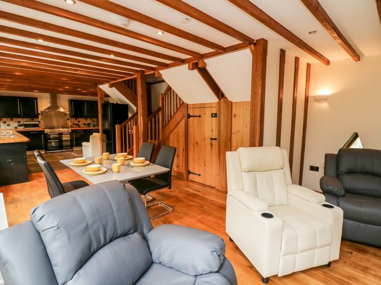 Cozy living area with recliners, a dining table set for six, and a view of the kitchen and wooden staircase, perfect for enjoying relaxed Ploony Holidays in the heart of Wales.