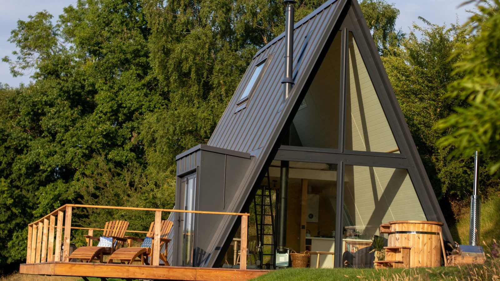 The Fold: an A-frame cabin with large windows, a wooden deck, and outdoor chairs, all beautifully enveloped by lush greenery.