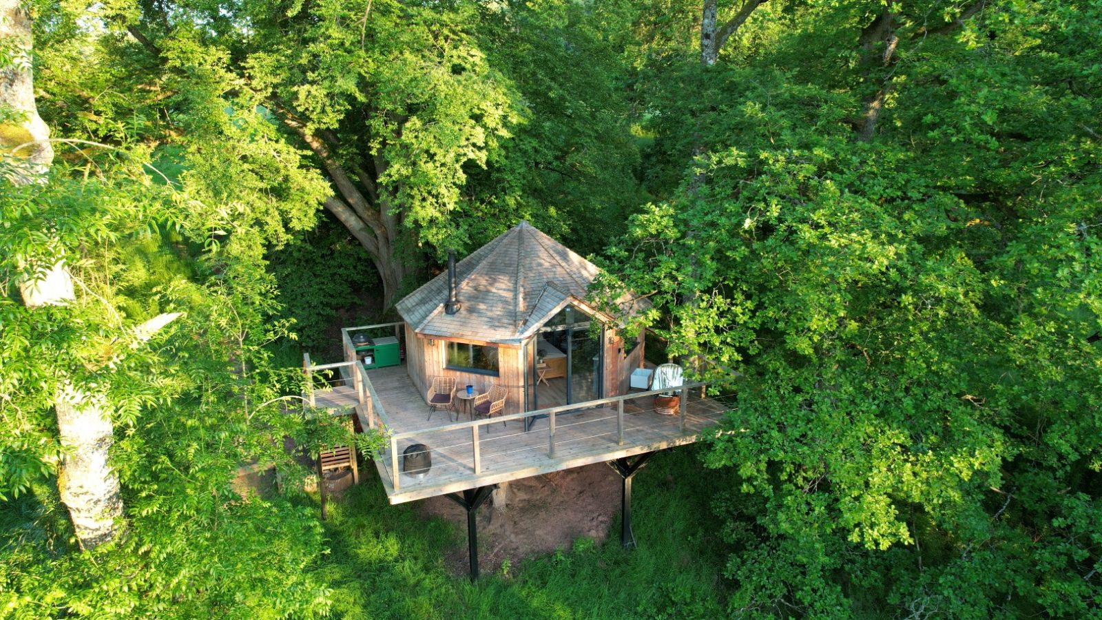 Nestled among lush green foliage, The Fold is a charming treehouse cabin. It boasts a wooden deck with a table and chairs, perfectly elevated among the trees for an enchanting escape.