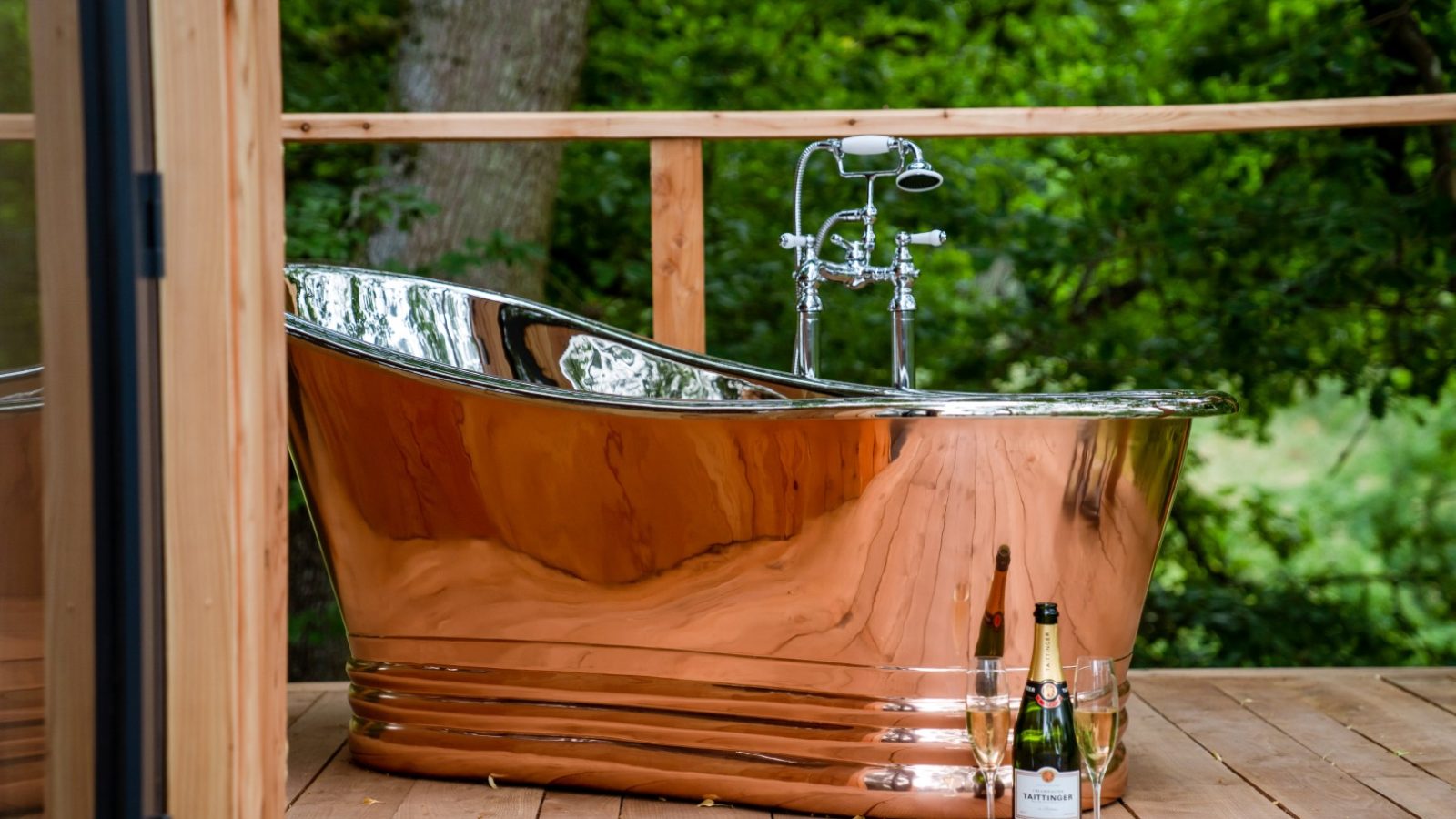 Perched on the wooden deck of a serene treehouse, a luxurious copper bathtub awaits. With champagne and glasses beside it, The Fold offers an intimate escape amidst the whispering trees.