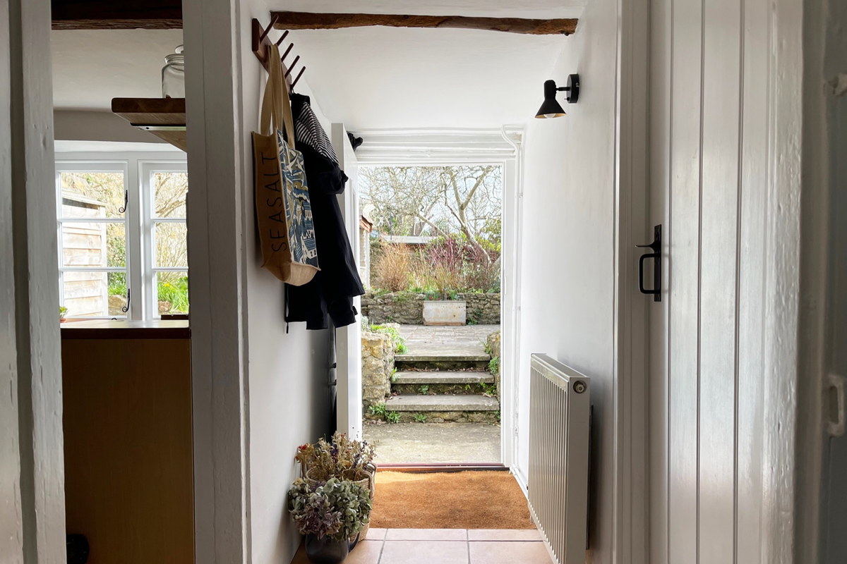 Bright hallway at Blackbird Cottage with white walls, a coat rack, and a potted plant, leading to garden steps and greenery.